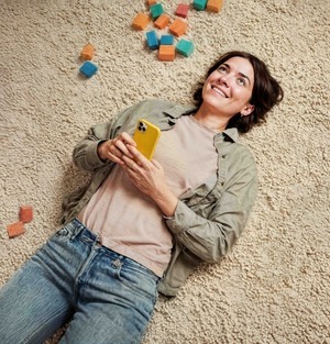 Vrouw ligt op vloerkleed met smartphone en kijkt blij